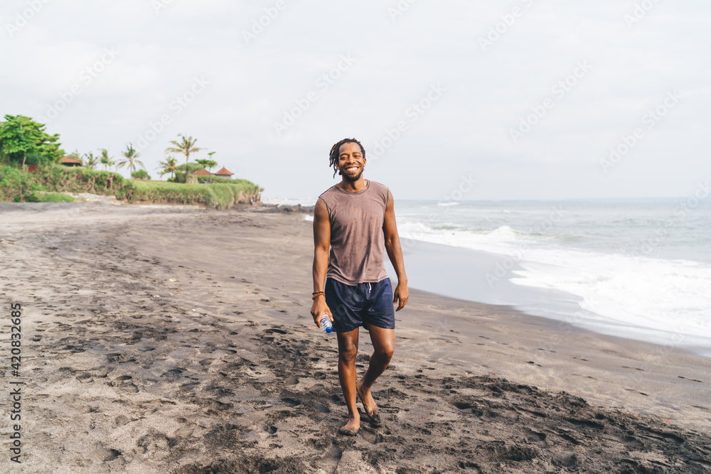 Happy black guy standing on sandy beach