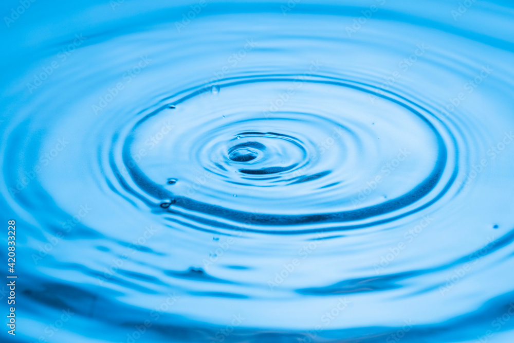 View macro of drops making circles on blue water surface isolated on background. View macro of drops making circles on blue water surface isolated on background.