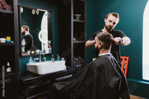 Professional hairdresser serves male client in barbershop