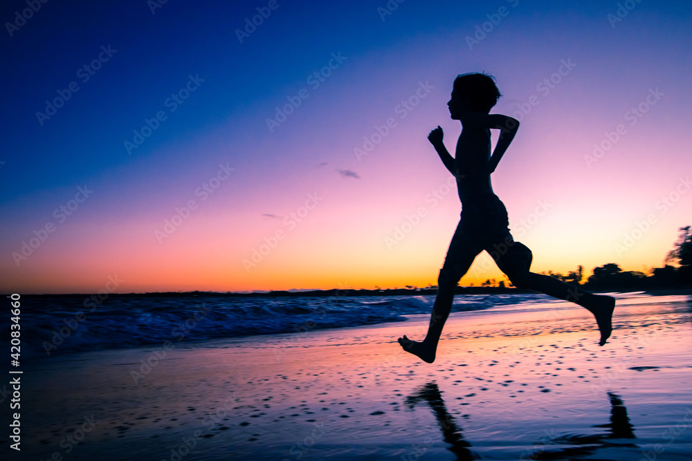 Silhueta de uma criança correndo em direção ao mar durante lusco fusco do pôr do sol em uma praia.