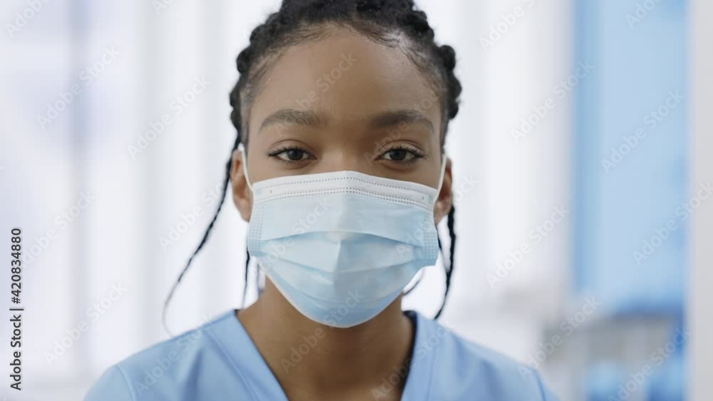 Close up view of woman in medical protective mask raising head and looking to camera. Portrait of female young medical worker with dreadlocks posing in hospital . Concept of health care. Close up view of woman in medical protective mask raising head and looking to camera. Portrait of female young medical worker with dreadlocks posing in hospital . Concept of health care.