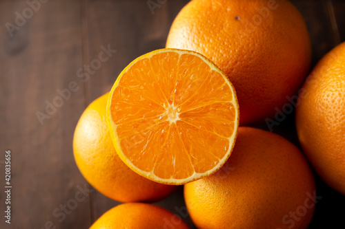 close up of a ripe orange cut in half and several whole oranges on brown rustic wooden table with copy space