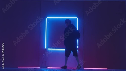 Person in windbreaker and red cap dancing to breakdance. blue rectangle neon background . Flickering neon background . man dancing to breakdance in night club