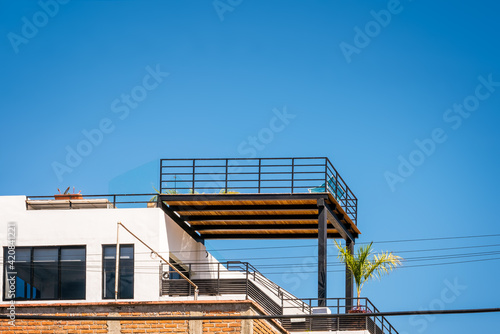 A modern apartment, condo exterior, with a rooftop terrace and balcony, patio furnishings against a clear blue tropical sky. Residential - concept, copy space. background