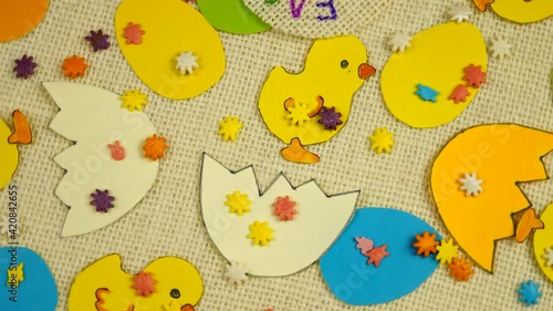 Multicolored Easter chickens and eggs made of colored paper lie on white burlap, handmade, decorative background