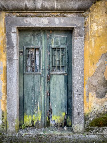 Derelict Weathered Wooden Doors With Chain. With Strong Stone Border And Yellow Peeling Wall, Braga, Portugal.