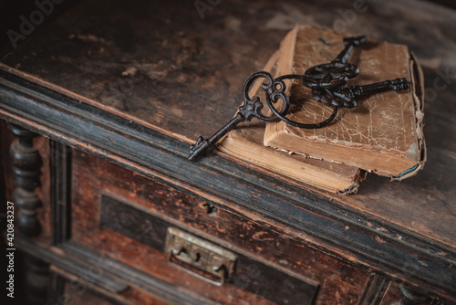 old vintage keys on an old battered book, antique wooden background. The concept of mystery and discovery, answers to questions, a clue. photo