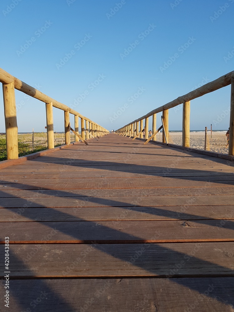 Ponte nova de madeira para acesso de pedestres à praia em um dia de céu azul

