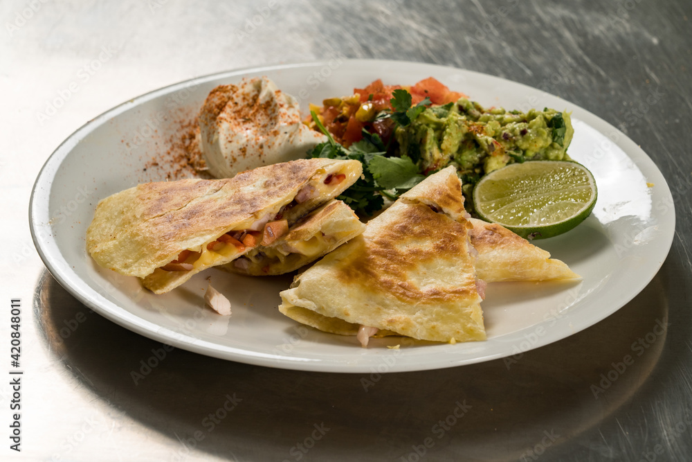 Close up shot of tortilla Mexican snack divided into pieces on white dish decorated with lime and spicy sauce