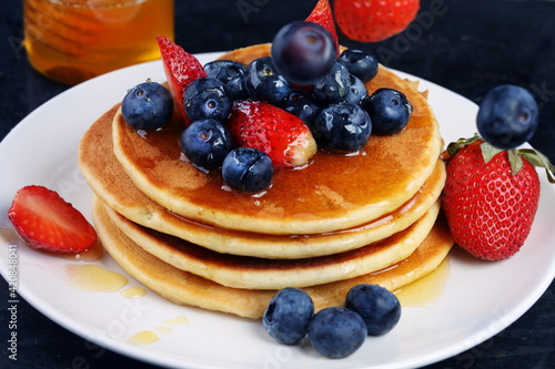 Pancakes with blueberries, strawberries, honey on a blue background