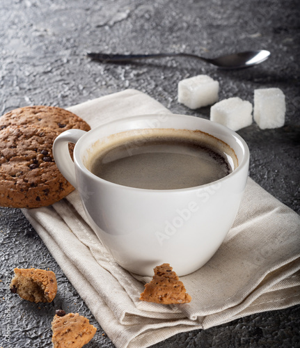 A cup of fresh coffee beans and cookies in the background. Espresso in a white coffee cup.