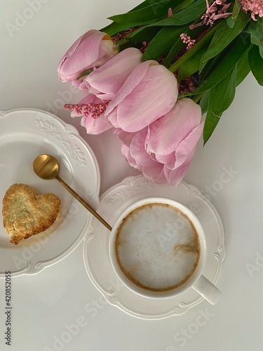 Morning breakfast with cup of coffee and biscuits in the background pink flower tulips