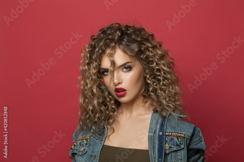 Portrait of attractive model woman with curly hairdo on red background. Young lady with trendy hair styling and hair dye