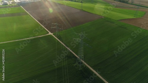 Drone view of electric supports against the sky among empty green and grey fields. The civilization is visable on the background. Sunny day, summer, countryside, high voltage line. 4K video. photo