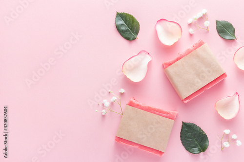 Handmade floral soap bars in a paper packaging with empty space. Bio soap for bath in craft wrapper with mockup made next to flowers and rose petals on a pink background. © Volha