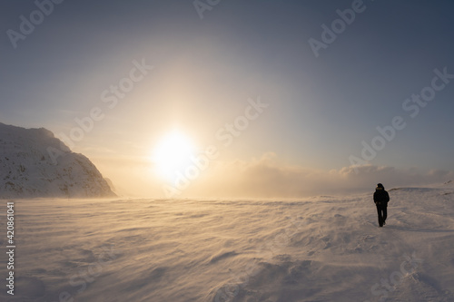 Scenic picture of large Sunset halo in winter mountains, selective focus because of strong snow drift wind. A person in black snowmobile overall and goggles walks against strong wind. Lapland Sweden © Alexandre Patchine