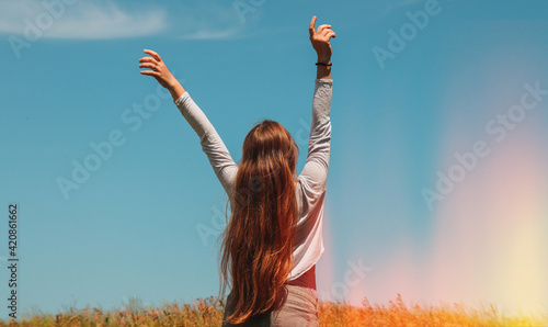 A long-haired blonde in the middle of a field with wheat raised her hands up and enjoys the air and freedom.