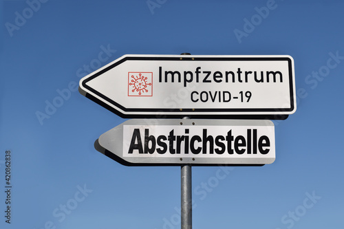 Traffic signs or arrows to vaccination against disease of virus covid-19 or coronavirus. Information or text in german language "Vaccination center covid-19" and "Place of test of smear". © igradesign
