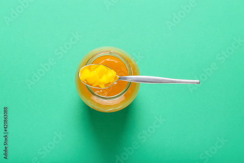 Jar with mango sauce on color background