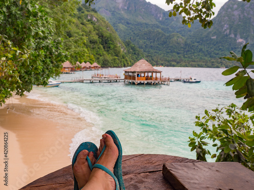 Ora Beach, Indonesia - Feb, 2018: Relax over the turquoise water. Woman feet over the wooden pond. Seram island, Central Maluku, Indonesia, Asia