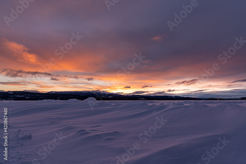 Winter frozen lake scene in northern Canada on a stunning cloudy sunset afternoon in March with white snow  mountains in background and iconic Canadian landscape in the north. 
