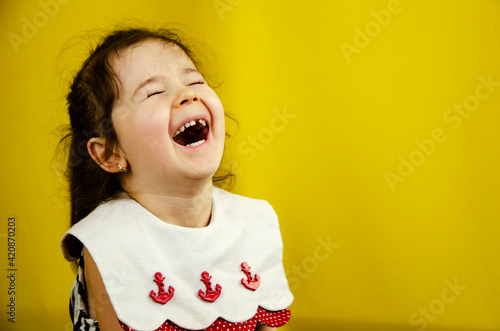 Happy child on a yellow background. Cheerful little girl laughs. Little girl in a dress on a yellow background. A cute little girl is spending time carefree. Children concept. A loving family. Joyful 