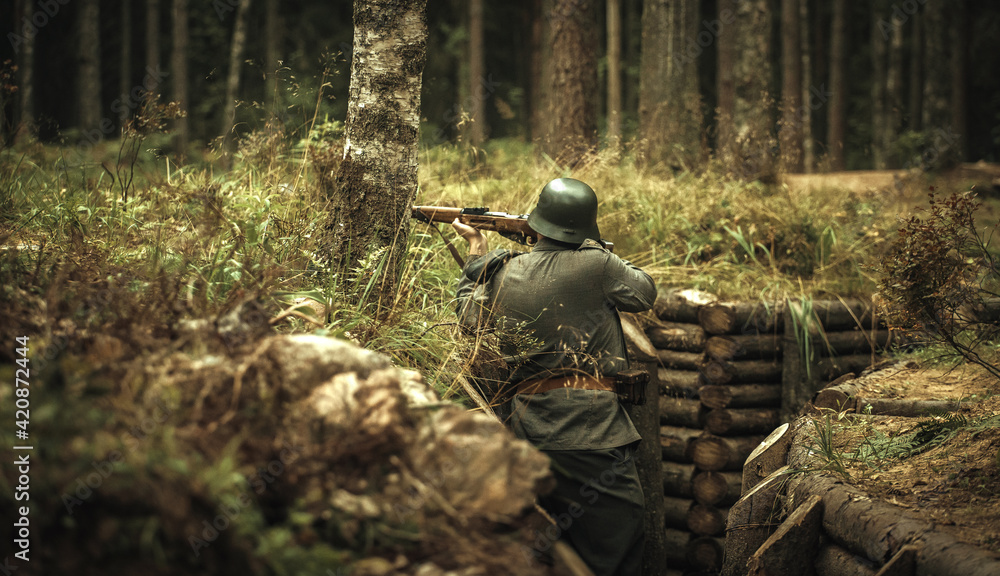 Finnish soldier of the Second World War, shooting from a trench in the forest. A steel helmet on his head and a rifle in his hands.