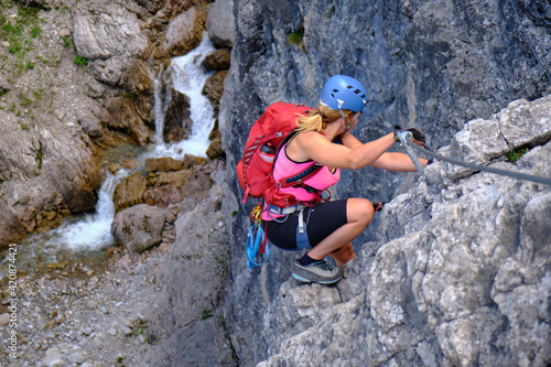 Woman tourist climbs Hanauer via ferrata route in Tirol, Austria, near a water stream. Adventure, tourism.