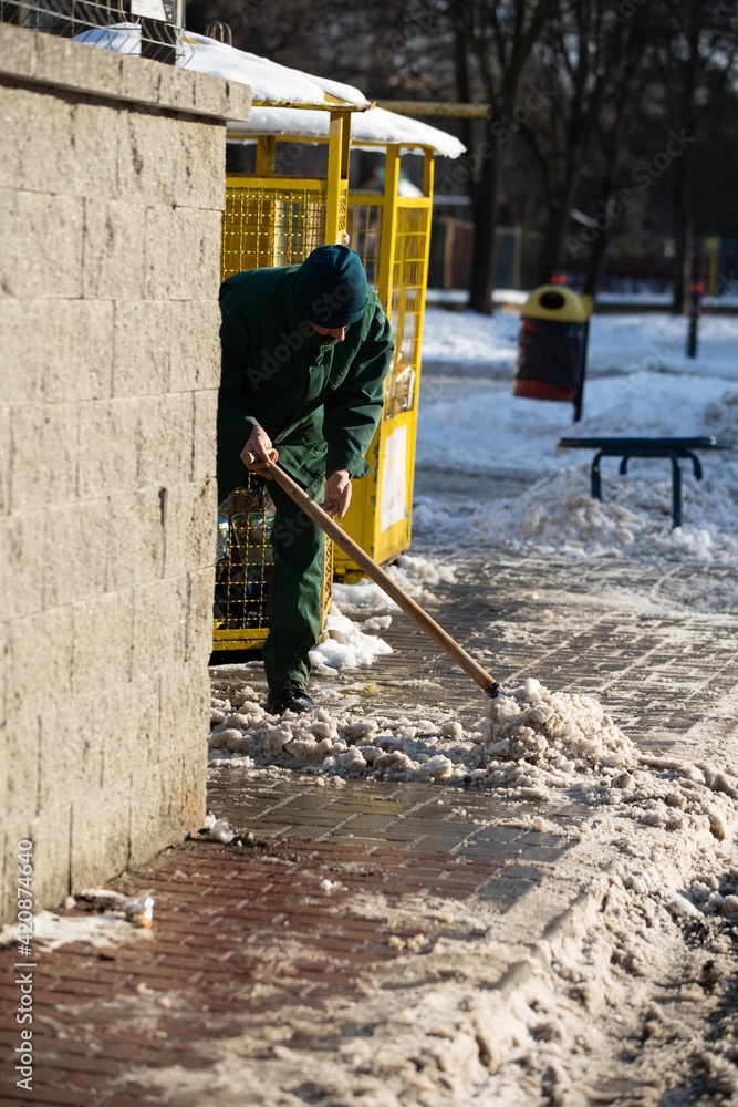 A manual worker scrapes snow off the pavement with a metal shovel A manual worker scrapes snow off the pavement with a metal shovel