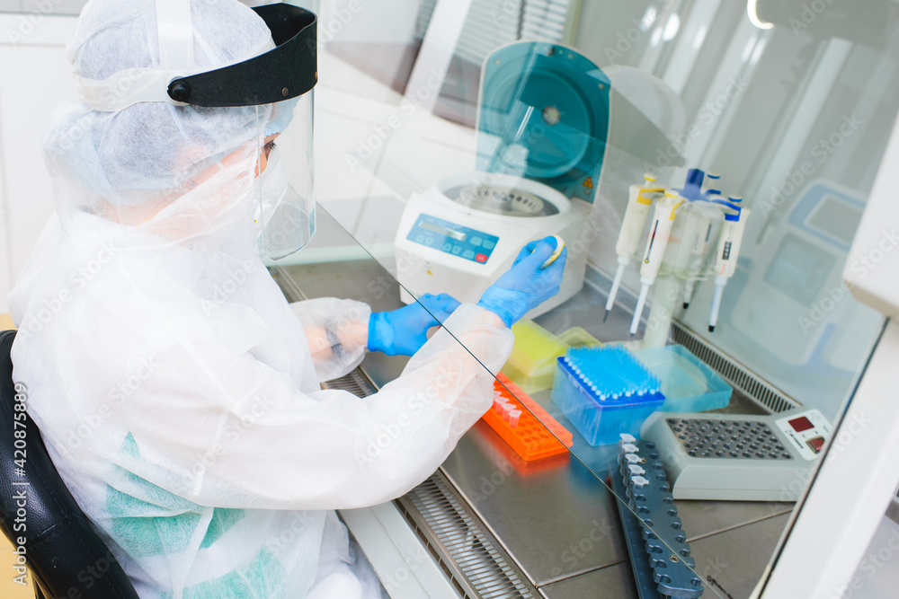 A researcher with a dispenser in his hands makes a scientific experiment against the background of ampoules with the inscription Vaccine. A researcher with a dispenser in his hands makes a scientific experiment against the background of ampoules with the inscription Vaccine.