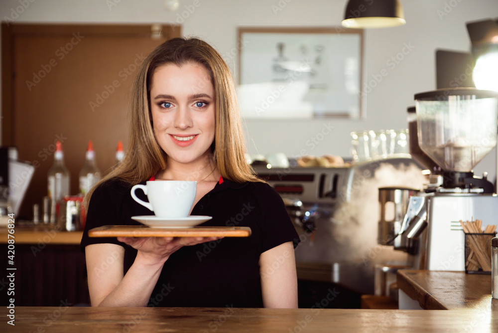 Beautiful female barista is working in coffee shop. Attractive woman is standing behind the bar counter, making coffee and welcomes customers. Beautiful female barista is working in coffee shop. Attractive woman is standing behind the bar counter, making coffee and welcomes customers.