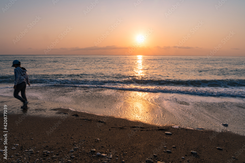A beach in south Turkey at sunrise time with sand and pebbles, and a child walking by in motion blur