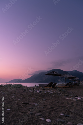 A beach in south Turkey with sunbeds and sunshades at dawn with a hazy atmosphere, mountain ranges and clouds in the background
