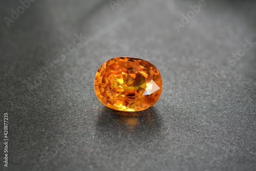 Natural mined, loose, oval faceted, orange color, transparent, beryllium heated, treated sapphire gemstone. Gray gradient textured backgound under dayligh from window made closeup photo. photo