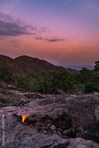 A sunset view from the Yanartaş hilltop in south Turkey with naturally burning fire in the foreground and the Mediterranean Sea in the background