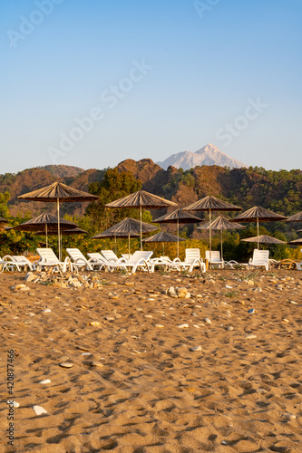 An image from a sandy and pebble stone beach in south Turkey with sunbeds and sunshades, a high mountain peak in the background