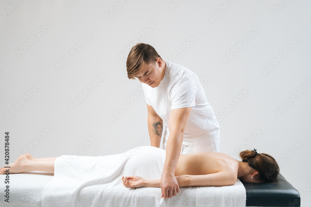 Side view of male masseur massaging hand of female lying on massage table at spa salon. Beautiful young woman with perfect skin getting relaxing massage on white background. Side view of male masseur massaging hand of female lying on massage table at spa salon. Beautiful young woman with perfect skin getting relaxing massage on white background.