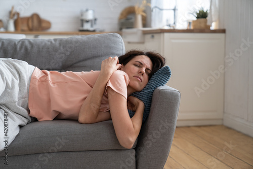 Young woman with closed eyes lying on pillow, resting, trying to sleep in uncomfortable pose on sofa at home, feel fatigue. Tired girl fall asleep, taking nap. 
