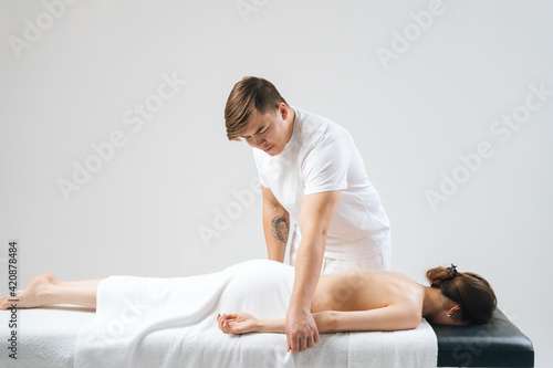 Side view of male masseur massaging hand of female lying on massage table at spa salon. Beautiful young woman with perfect skin getting relaxing massage on white background.