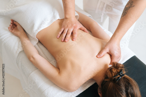 Top view of male masseur doing back massage to young unrecognizable woman in spa salon. Professional physiotherapist with strong hands making movements with hand along the spine toward head.