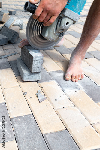 A worker cuts paving slabs with a grinder for subsequent laying, vertical shot.
