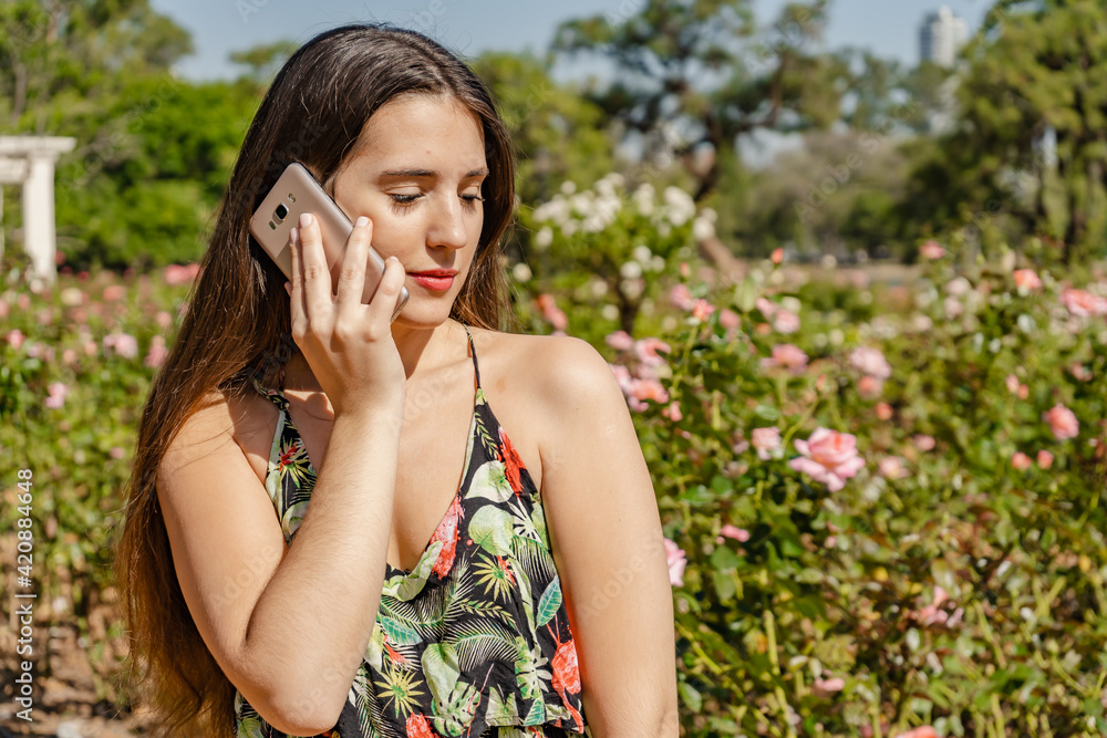 Beautiful young Latin woman in a park talking on her cell phone. Technology and communication concept. Beautiful young Latin woman in a park talking on her cell phone. Technology and communication concept.