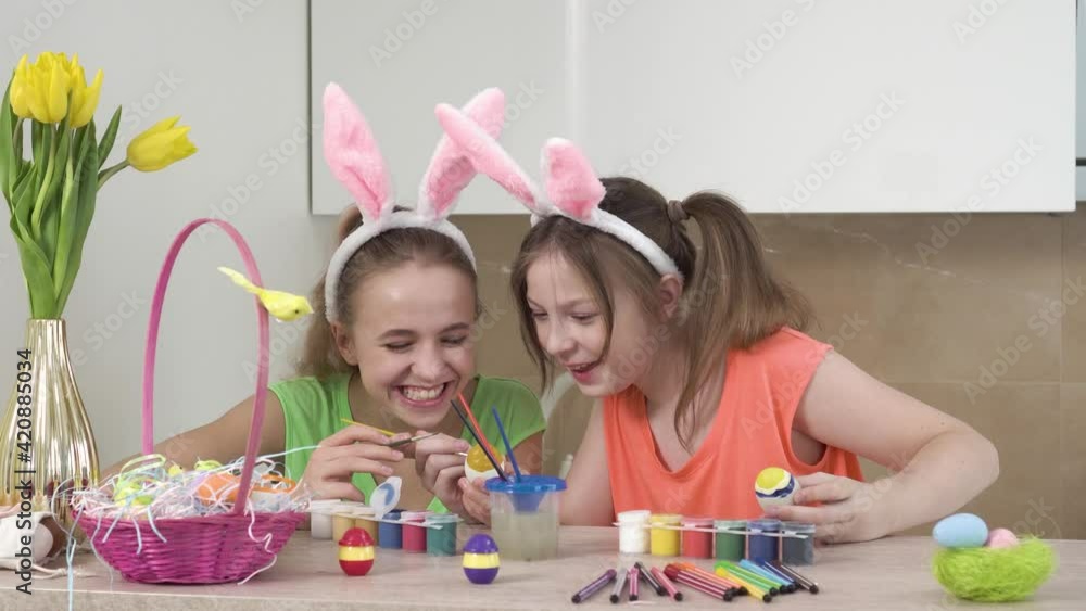 Girls decorate Easter eggs and help each other, talk and laugh. On the table is an Easter basket with eggs. Easter holiday. Girls decorate Easter eggs and help each other, talk and laugh. On the table is an Easter basket with eggs. Easter holiday.