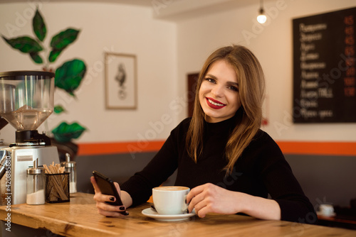 happy Caucasian female watching her photo on cell telephone while relaxing in cafe.