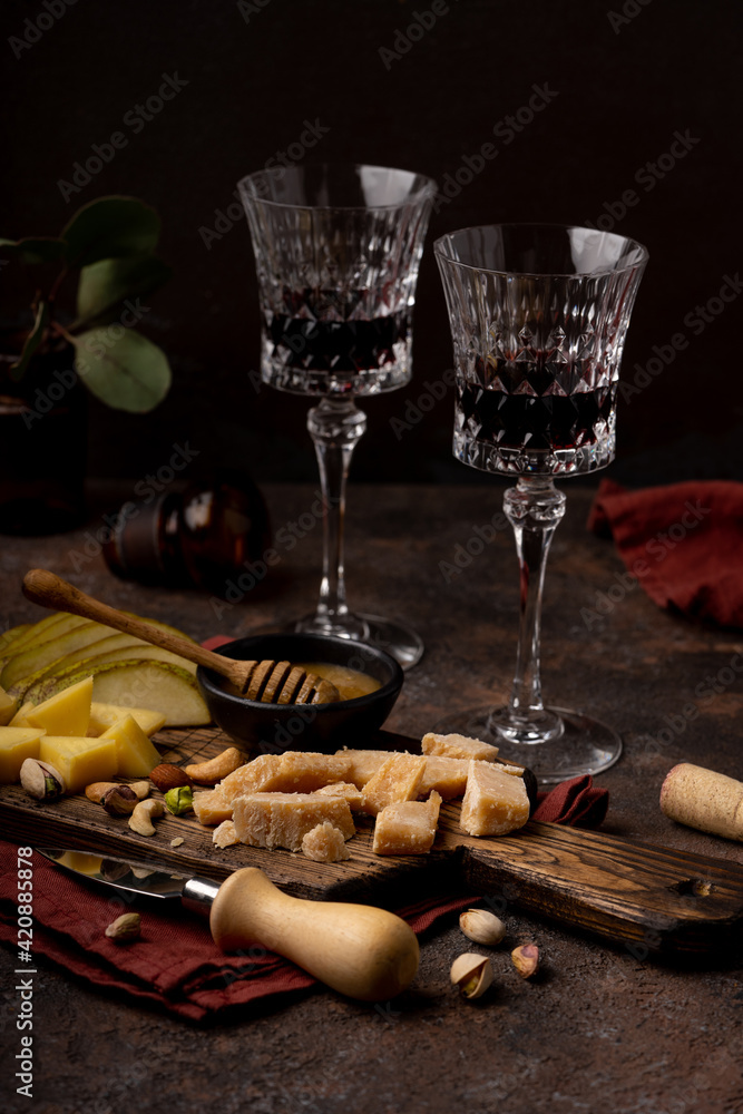 Cheese platter with different cheeses, sliced pear, nuts and honey and glasses of red wine on rustic wooden background. Retro styled cheese variety selection on wood board. Selective focus. High