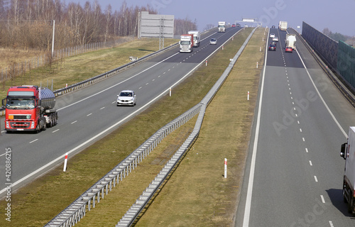 Various vehicles traveling on the highway. Visible sound-absorbing barriers separating the motorway from the residential area.