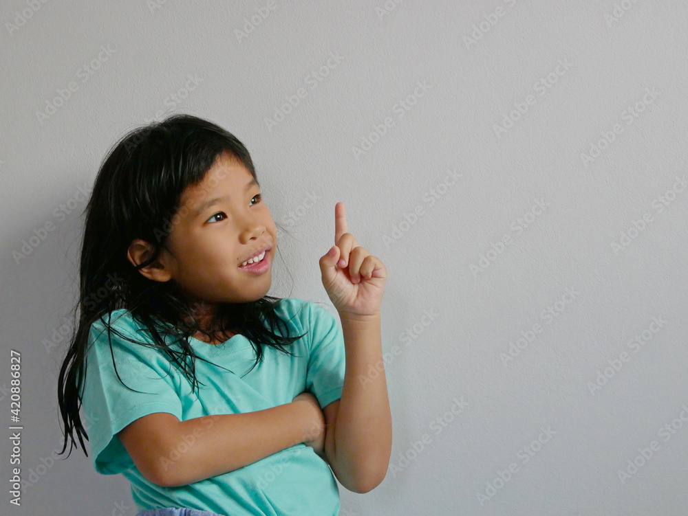 A side-shot portrait of surprised, excited, little girl, 5 years old, pointing her finger up on a white blank background, copy space A side-shot portrait of surprised, excited, little girl, 5 years old, pointing her finger up on a white blank background, copy space