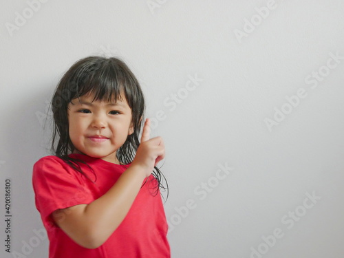 A portrait of smiling little girl, 4 years old, pointing her finger up on a white blank background, copy space