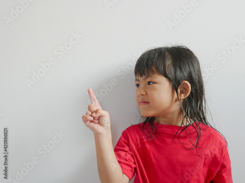 A side-view portrait of smiling little girl, 4 years old, pointing her finger up on a white blank background, copy space