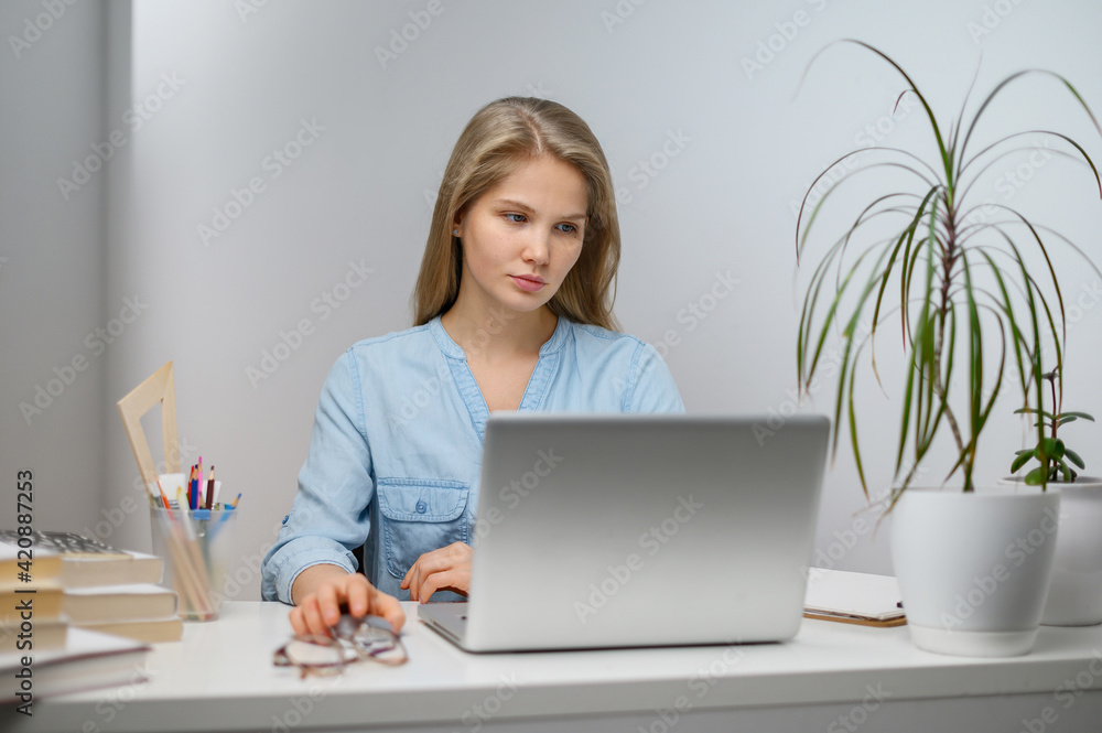 A girl with a laptop is studying at an online school. White room background